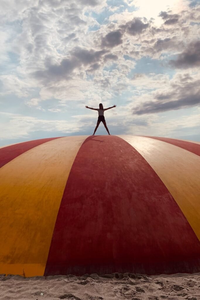 Person triumphantly standing atop a colorful playground dome at dusk, capturing a dramatic sky.