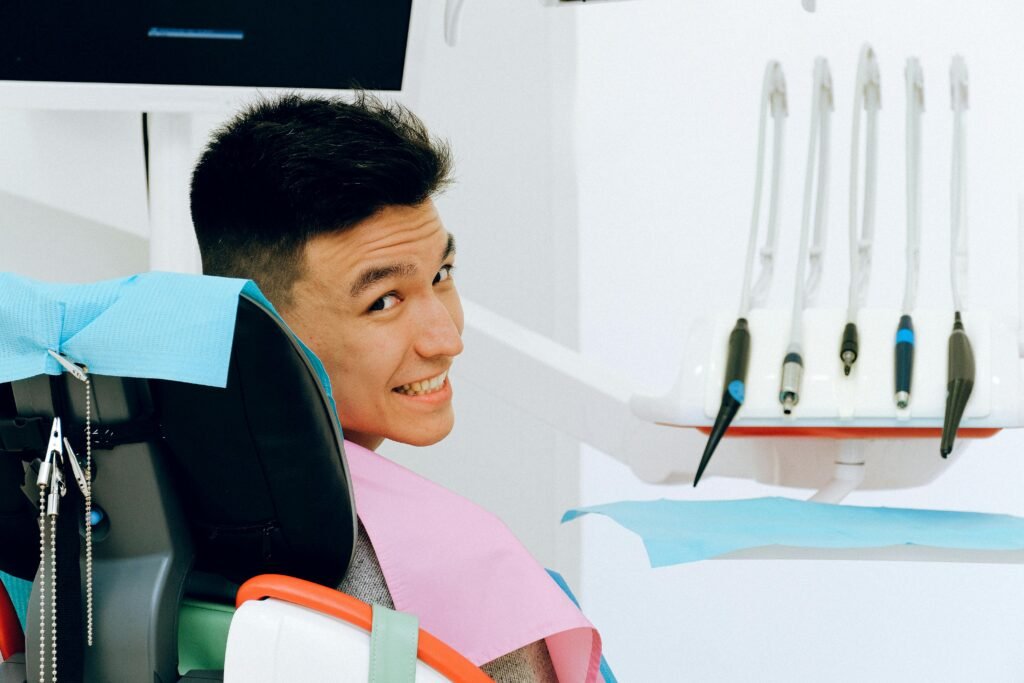 Back view of smiling ethnic man sitting in chair of dentist while preparing for treatment in modern clinic and looking over shoulder at camera